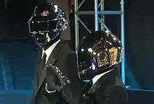 Two men wearing grey jumpsuits and robot helmets.