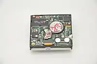 DataPlay optical drive engine bottom (same as No.3) The large coin-like object is a motor for spinning the disc, and the metal piece at its left is a magnet;  the laser pickup of the drive is mounted on an arm that is moved using a mechanism, the latter two of which are reminiscent of that of modern hard disks.